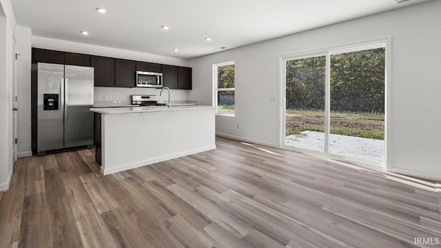 kitchen featuring light hardwood / wood-style flooring, an island with sink, dark brown cabinets, and appliances with stainless steel finishes