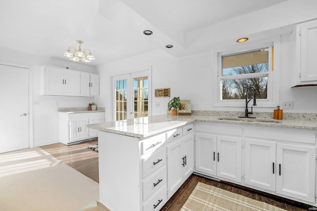 kitchen with kitchen peninsula, light stone counters, white cabinetry, and sink