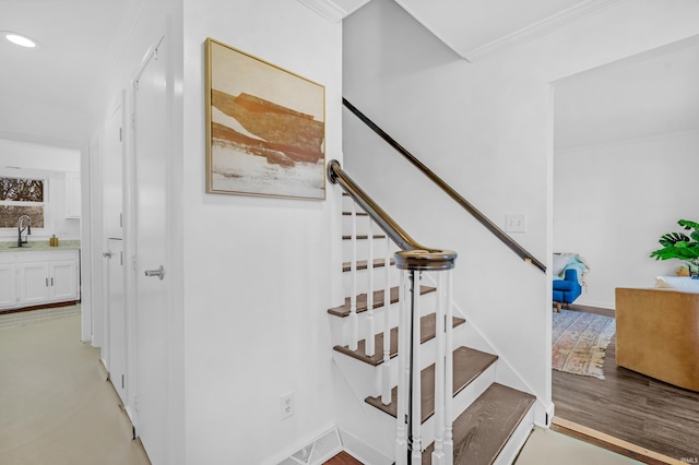 staircase with wood-type flooring, crown molding, and sink