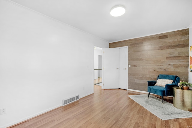 living area with wooden walls, light hardwood / wood-style flooring, and crown molding