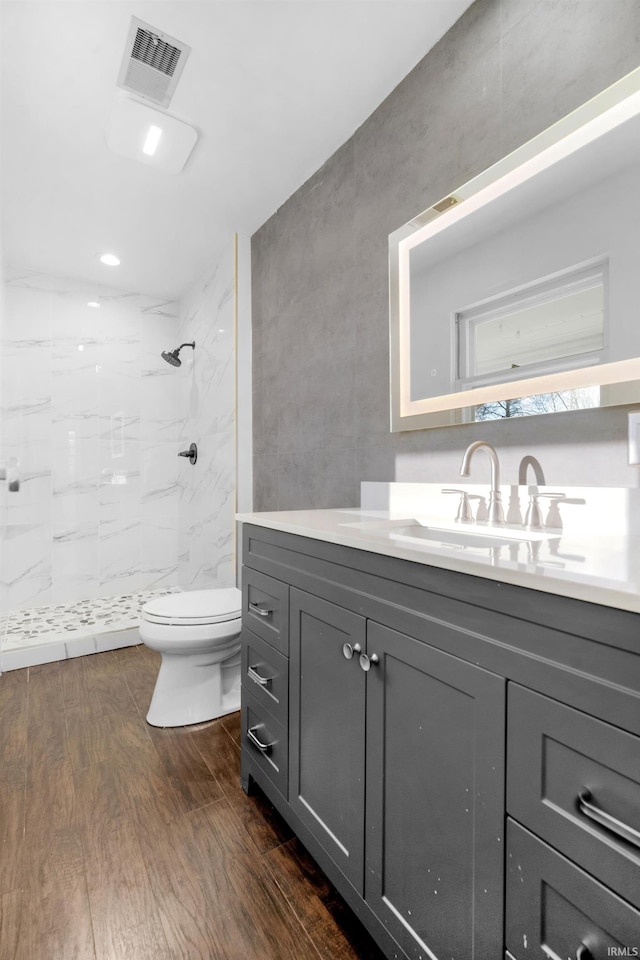 bathroom with a tile shower, vanity, hardwood / wood-style flooring, and toilet