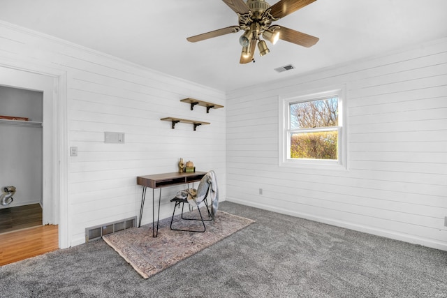 carpeted home office with ceiling fan, ornamental molding, and wood walls