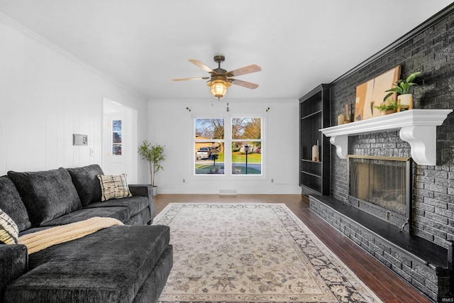 living room with dark hardwood / wood-style floors, ceiling fan, crown molding, and a brick fireplace