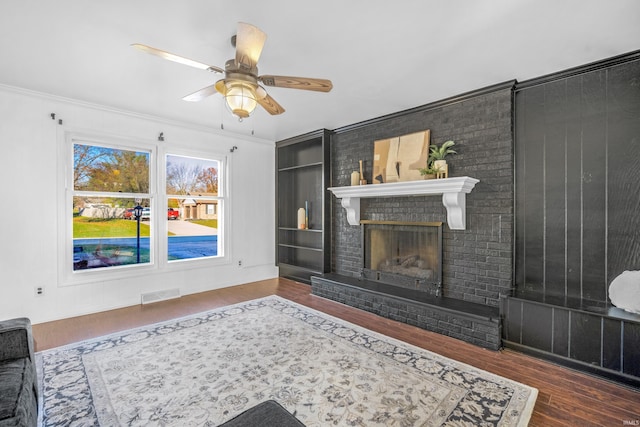 living room featuring ceiling fan, ornamental molding, dark wood-type flooring, and a brick fireplace