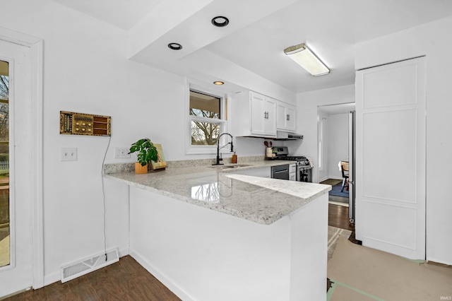 kitchen with light stone countertops, stainless steel range, sink, kitchen peninsula, and white cabinets