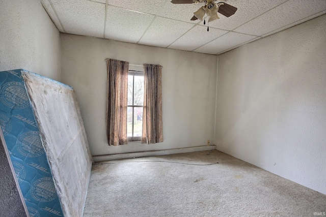 carpeted spare room with ceiling fan and a drop ceiling