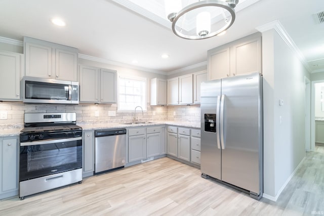 kitchen with light wood-type flooring, stainless steel appliances, ornamental molding, and sink