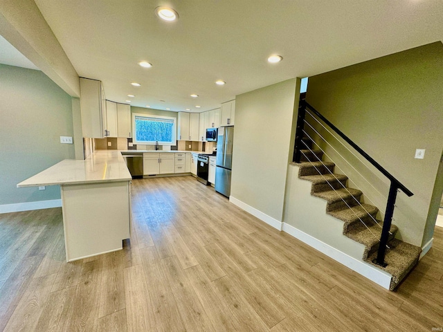 kitchen with kitchen peninsula, stainless steel appliances, sink, white cabinets, and light hardwood / wood-style floors