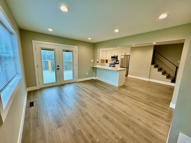 interior space featuring kitchen peninsula, appliances with stainless steel finishes, light wood-type flooring, french doors, and white cabinets