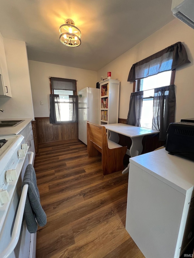 kitchen with wood walls, white appliances, sink, dark hardwood / wood-style floors, and white cabinetry