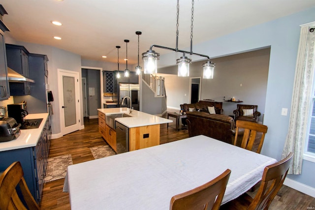 kitchen with sink, stainless steel dishwasher, dark hardwood / wood-style floors, pendant lighting, and a center island with sink