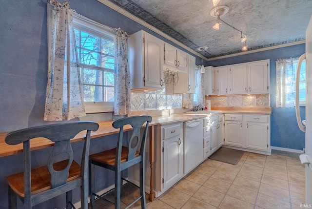 kitchen featuring dishwasher, tasteful backsplash, light tile patterned flooring, crown molding, and white cabinets