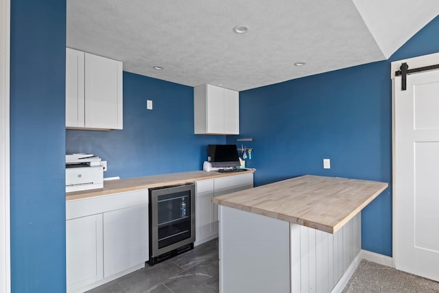 kitchen featuring kitchen peninsula, a textured ceiling, beverage cooler, a barn door, and white cabinetry