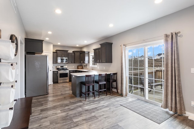 kitchen with kitchen peninsula, appliances with stainless steel finishes, a breakfast bar, sink, and light hardwood / wood-style flooring