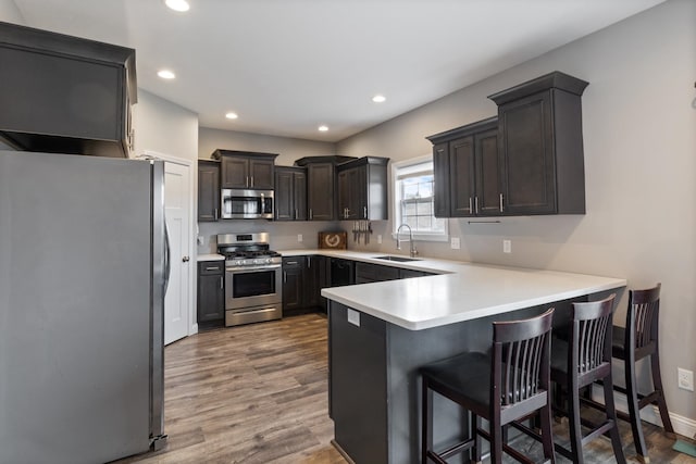 kitchen with kitchen peninsula, appliances with stainless steel finishes, sink, wood-type flooring, and a breakfast bar area