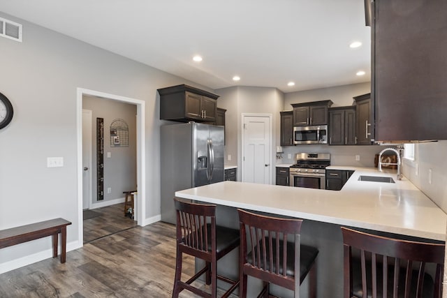 kitchen featuring sink, dark wood-type flooring, kitchen peninsula, a breakfast bar area, and appliances with stainless steel finishes