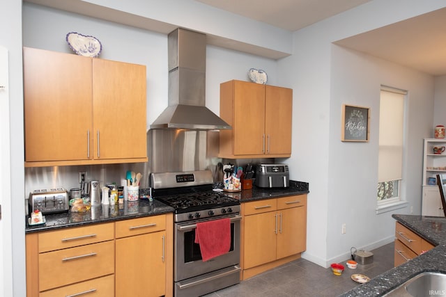 kitchen with dark tile patterned floors, gas stove, wall chimney range hood, and dark stone counters