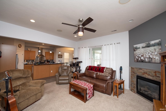 carpeted living room featuring ceiling fan, a stone fireplace, and a textured ceiling