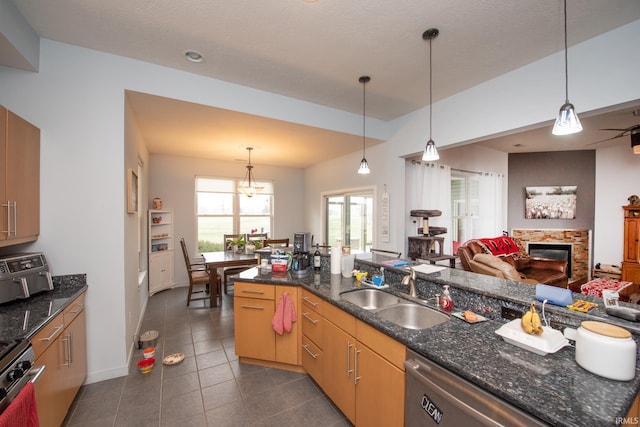 kitchen with dishwashing machine, sink, dark tile patterned floors, hanging light fixtures, and dark stone counters