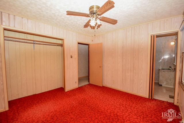 unfurnished bedroom with ceiling fan, a closet, wood walls, and dark colored carpet