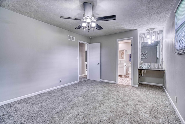 unfurnished bedroom with carpet, ceiling fan, a textured ceiling, and ensuite bath