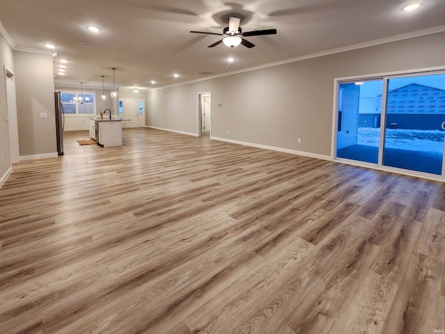 unfurnished living room featuring ceiling fan with notable chandelier, light wood-type flooring, and crown molding