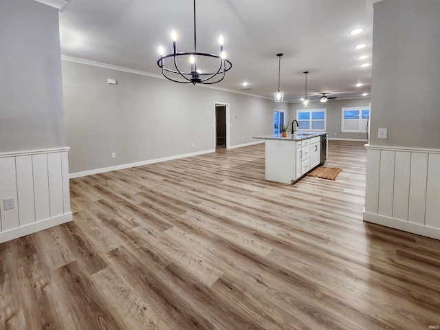 kitchen with hanging light fixtures, light hardwood / wood-style floors, a kitchen island with sink, ceiling fan with notable chandelier, and ornamental molding