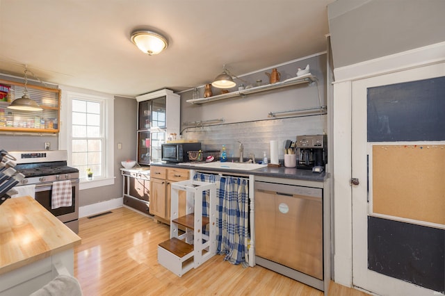 kitchen with butcher block counters, sink, tasteful backsplash, light hardwood / wood-style flooring, and appliances with stainless steel finishes