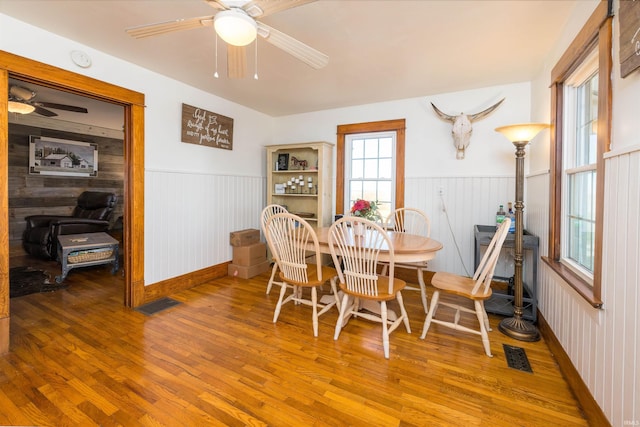 dining area with wooden walls, ceiling fan, and wood-type flooring