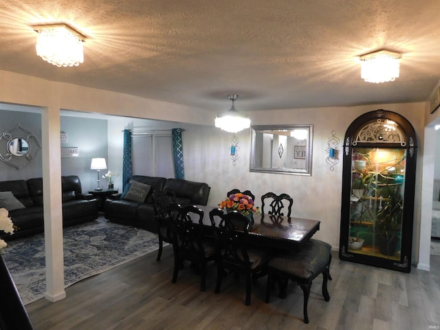 dining area with hardwood / wood-style floors, a textured ceiling, and an inviting chandelier