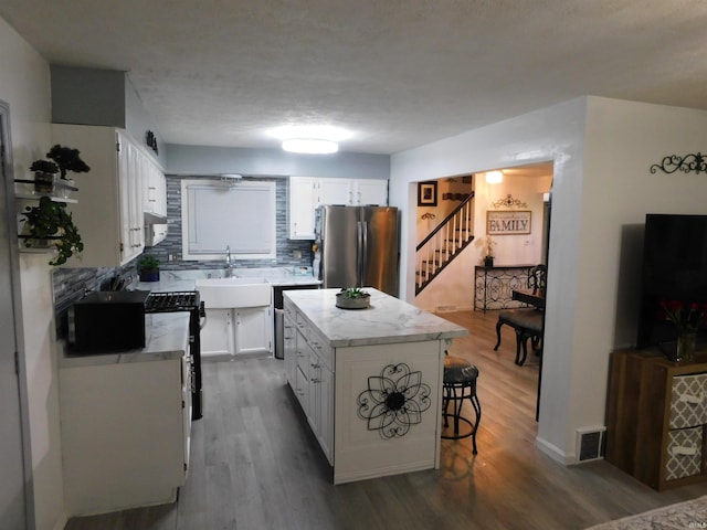 kitchen with a kitchen island, sink, hardwood / wood-style flooring, white cabinetry, and stainless steel refrigerator