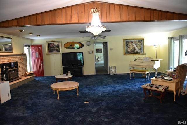 carpeted living room featuring ceiling fan, a fireplace, wooden walls, and vaulted ceiling