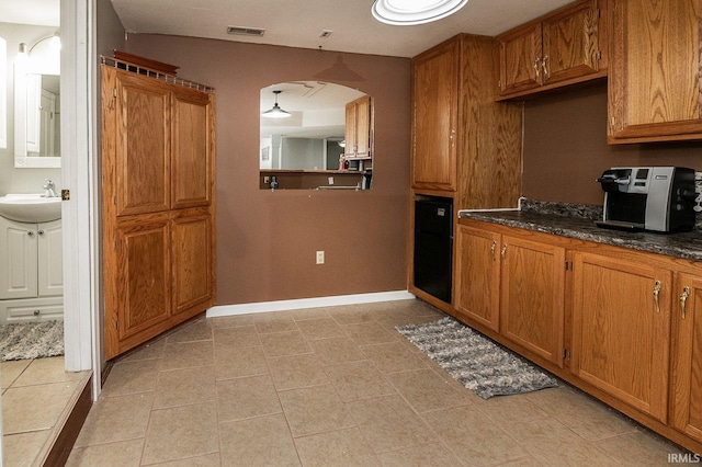 kitchen with black oven, light tile patterned floors, and sink