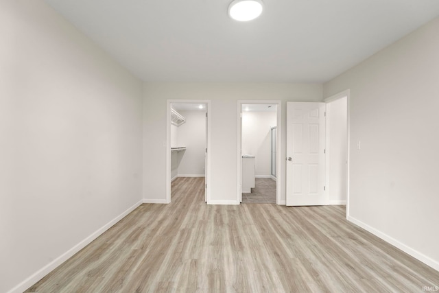 unfurnished bedroom with a closet, a spacious closet, and light hardwood / wood-style flooring