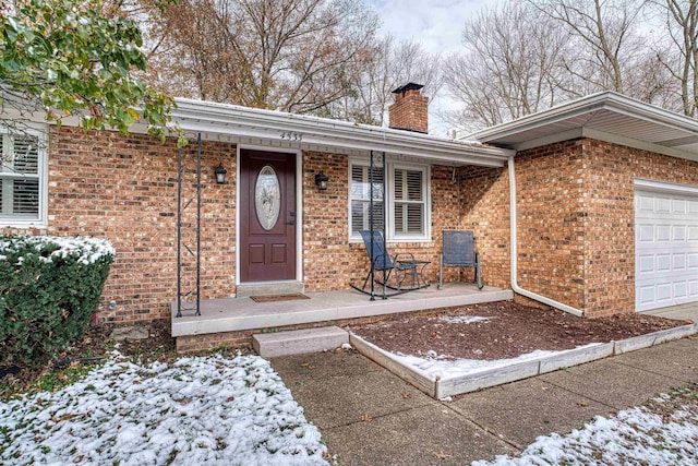 snow covered property entrance featuring a porch and a garage