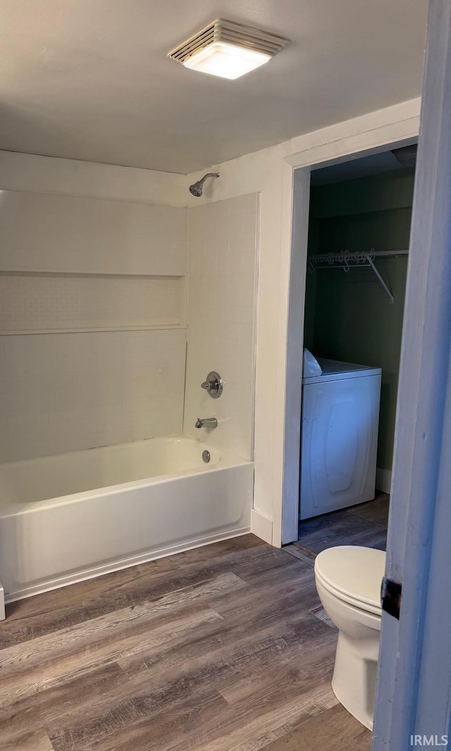 bathroom featuring washer / dryer, toilet, shower / bathtub combination, and hardwood / wood-style floors