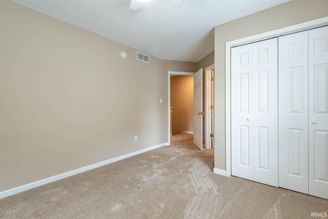 unfurnished bedroom with light carpet, a textured ceiling, a closet, and ceiling fan