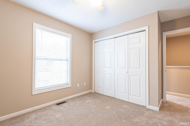 unfurnished bedroom featuring ceiling fan, a closet, light colored carpet, and multiple windows