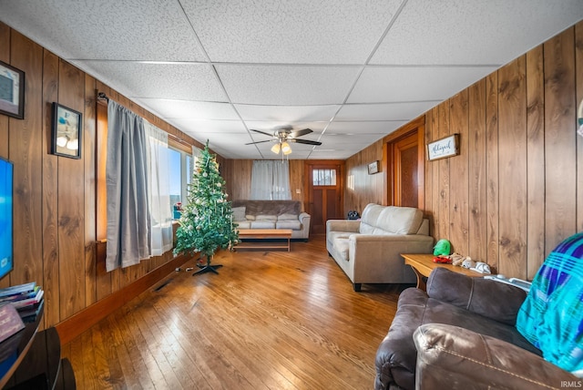 living room with hardwood / wood-style floors, a paneled ceiling, and wooden walls