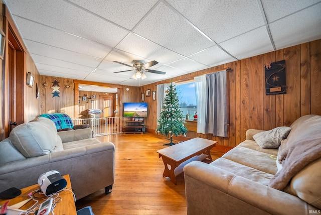 living room with a paneled ceiling, wood walls, light hardwood / wood-style flooring, and ceiling fan