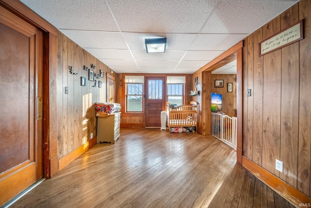 interior space with a paneled ceiling, light hardwood / wood-style floors, and wooden walls