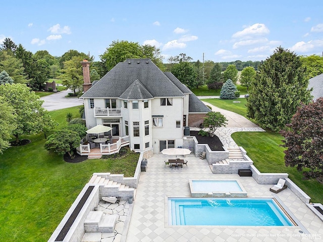 back of property featuring a lawn, a patio area, a balcony, and a fenced in pool