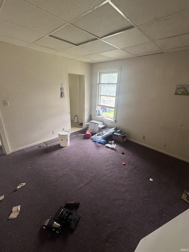 carpeted empty room featuring a paneled ceiling and baseboards