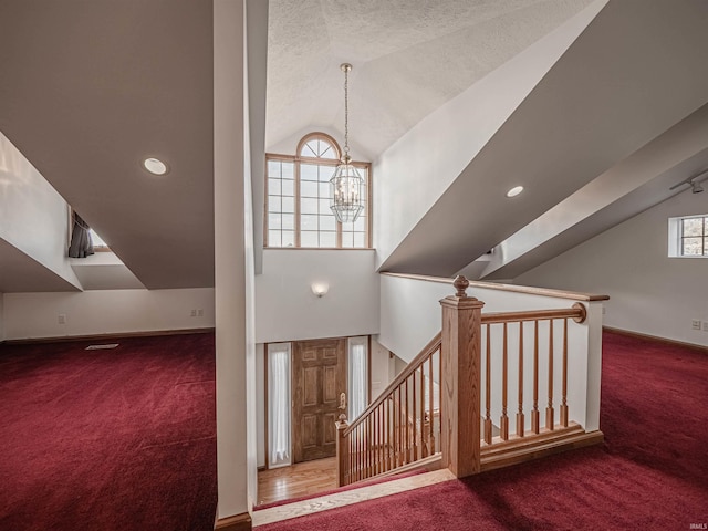 stairway with a chandelier, a textured ceiling, carpet floors, and vaulted ceiling