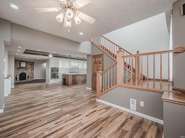 unfurnished living room with a textured ceiling, light hardwood / wood-style floors, a stone fireplace, and ceiling fan