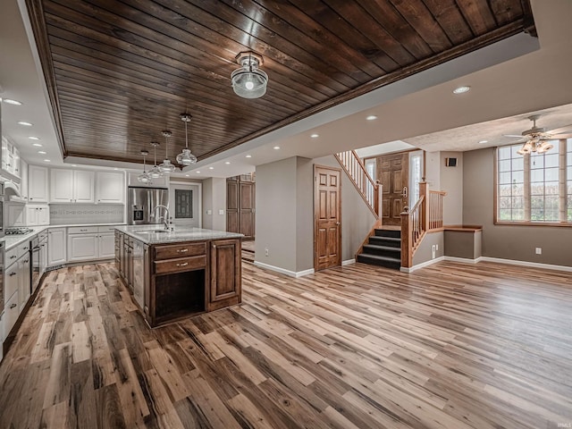 kitchen featuring light hardwood / wood-style floors, white cabinetry, a kitchen island with sink, and a tray ceiling