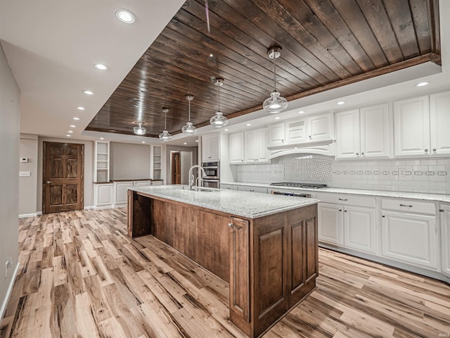 kitchen with pendant lighting, an island with sink, tasteful backsplash, light hardwood / wood-style floors, and white cabinetry