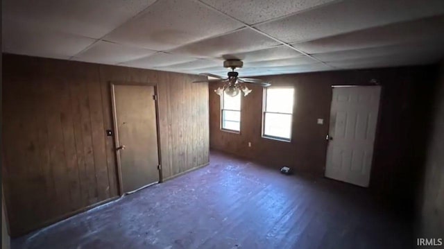 interior space with a paneled ceiling, ceiling fan, and wooden walls