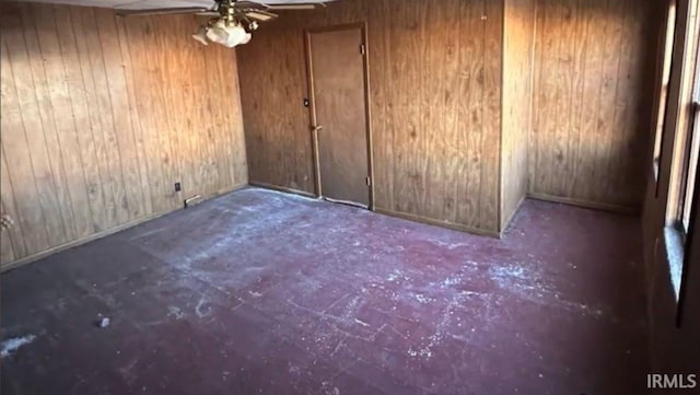 empty room with ceiling fan and wood walls