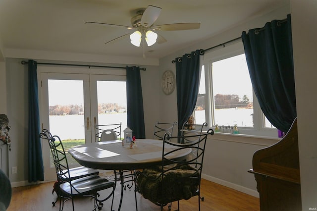 dining space featuring french doors, light wood-type flooring, a water view, and ceiling fan